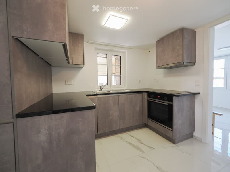 Modern kitchen with grey cabinets, white marble flooring, and stainless steel appliances including a sink, faucet, and oven.