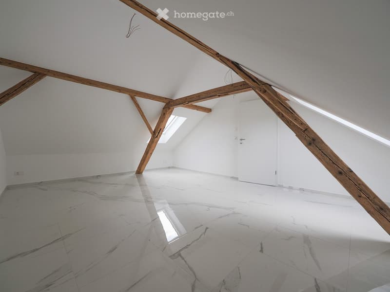 Empty attic space with exposed wooden beams, white walls, and a polished marble floor. Skylights allow natural light to enter.