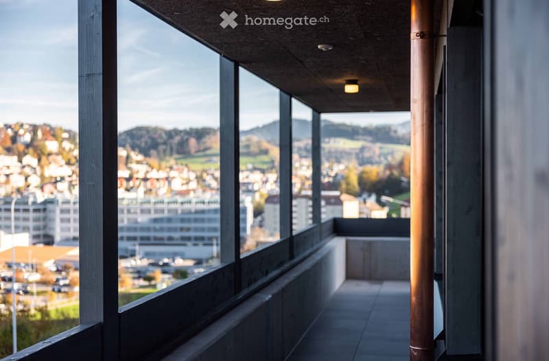 A balcony with a view of the city and mountains, featuring a tiled floor and a copper pipe.