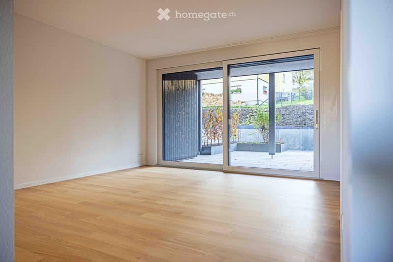 Empty room with white walls, wooden floor, and sliding glass doors leading to a patio.