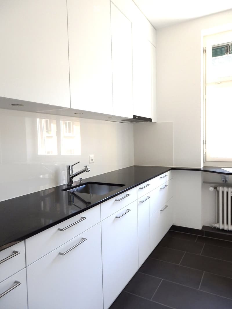 Modern kitchen with white cabinets, black countertops, and stainless steel sink and faucet.