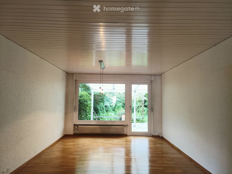 Empty room with wooden flooring, white walls, large window and door leading outside, radiator, and a hanging light fixture.