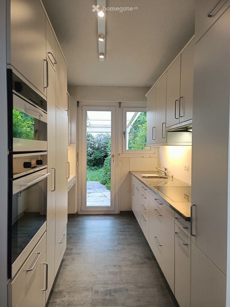 Modern kitchen with white cabinets, stainless steel appliances, and a large window overlooking a garden.