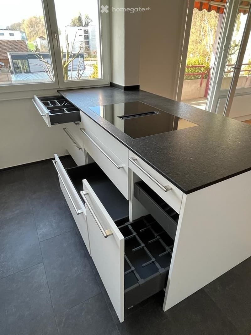Modern kitchen island with white cabinets, black countertop, and multiple open drawers.