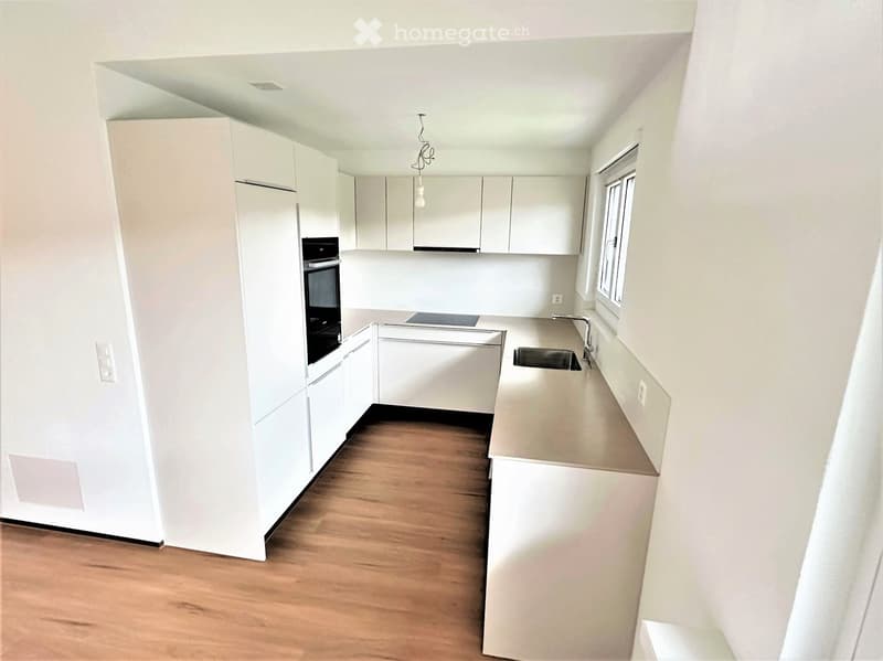 Modern, minimalist kitchen with white cabinets, a central island, and a wooden floor.