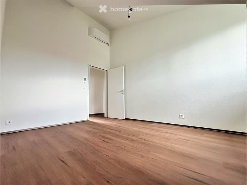 Empty room with wooden flooring, white walls, and a single open door leading to another space.