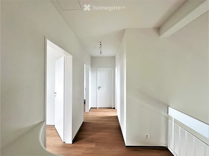 Empty hallway with light-colored walls, wooden flooring, and several white doors leading to rooms.