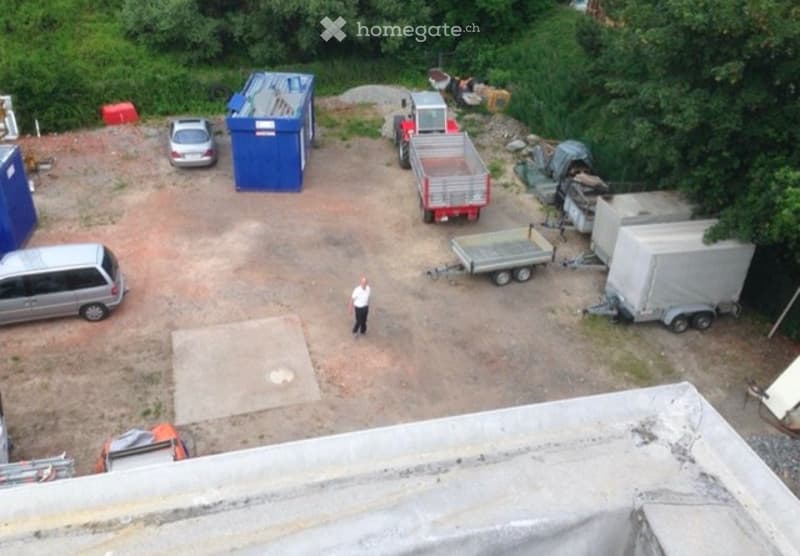 Aerial view of a parking area with several vehicles, including vans, trailers, and a dumpster, surrounded by greenery.