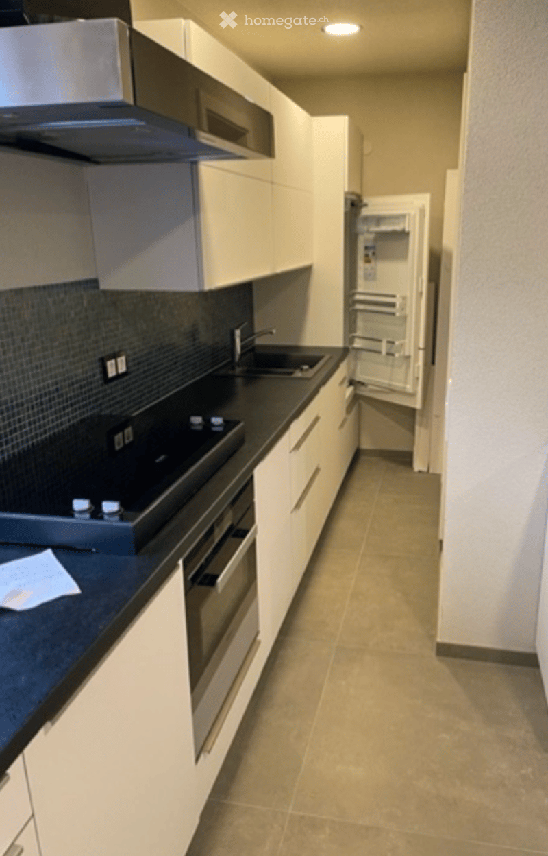Modern kitchen with white cabinets, black countertops, and stainless steel appliances including a stove, sink, and open fridge.