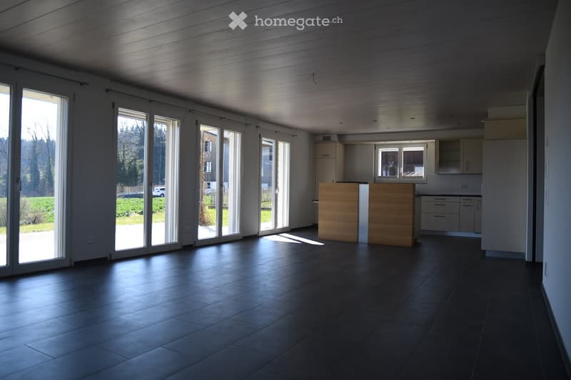 Open-plan space with dark tiled floor, large sliding glass doors leading outside, kitchen area with island and cabinets.