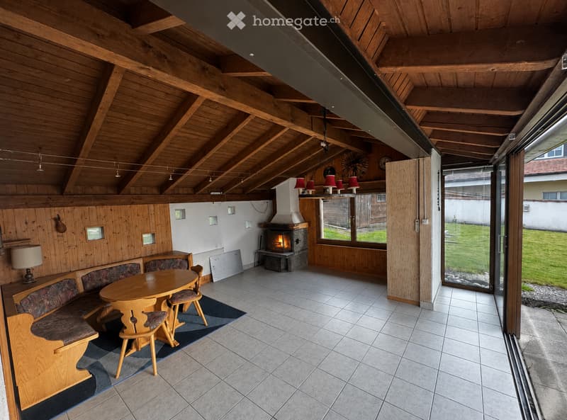 Furnished Room. Cozy living room with wooden beams, fireplace, sofa, dining table, and chairs.