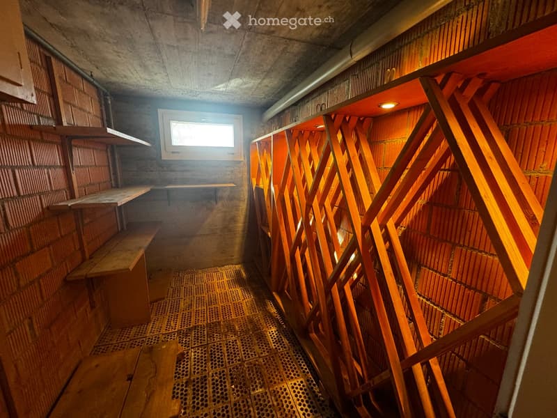 Corridor / Hallway. A narrow, dimly lit corridor with concrete walls, wooden benches, and a metal grated floor. A small window allows natural light to enter.