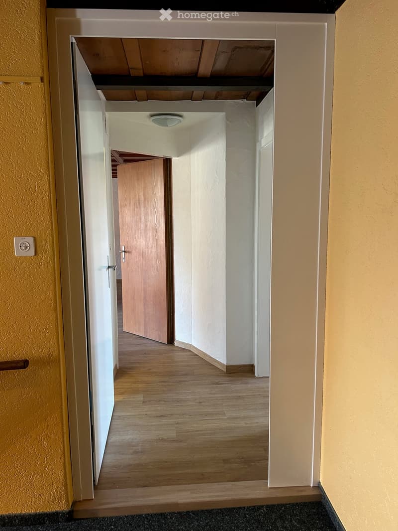Empty hallway with wooden flooring, white walls, and a partially open wooden door leading to another room.