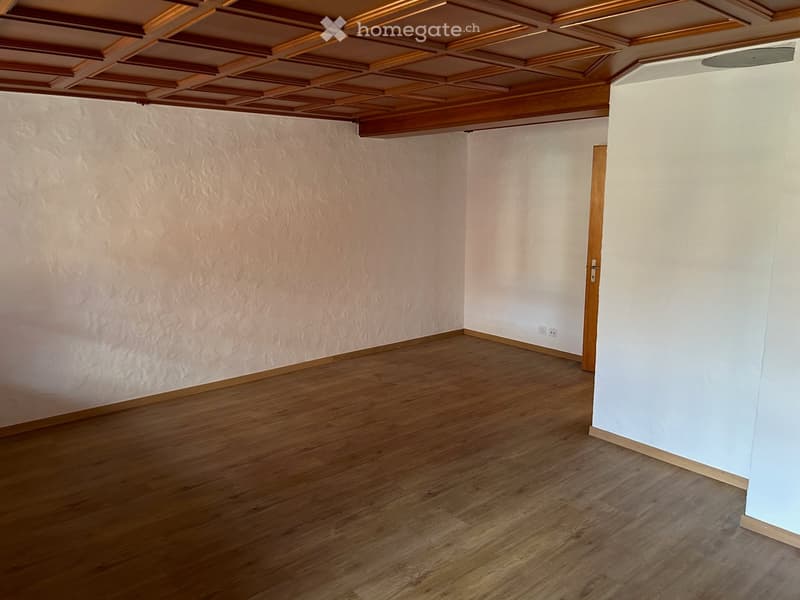 Empty room with wooden flooring, white walls, and a wooden door. The ceiling features a decorative wooden panel design.