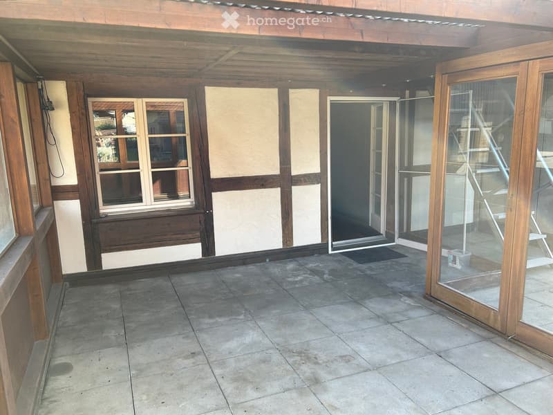 Wooden-framed balcony with tiled floor, large windows, and sliding glass doors leading to the interior.