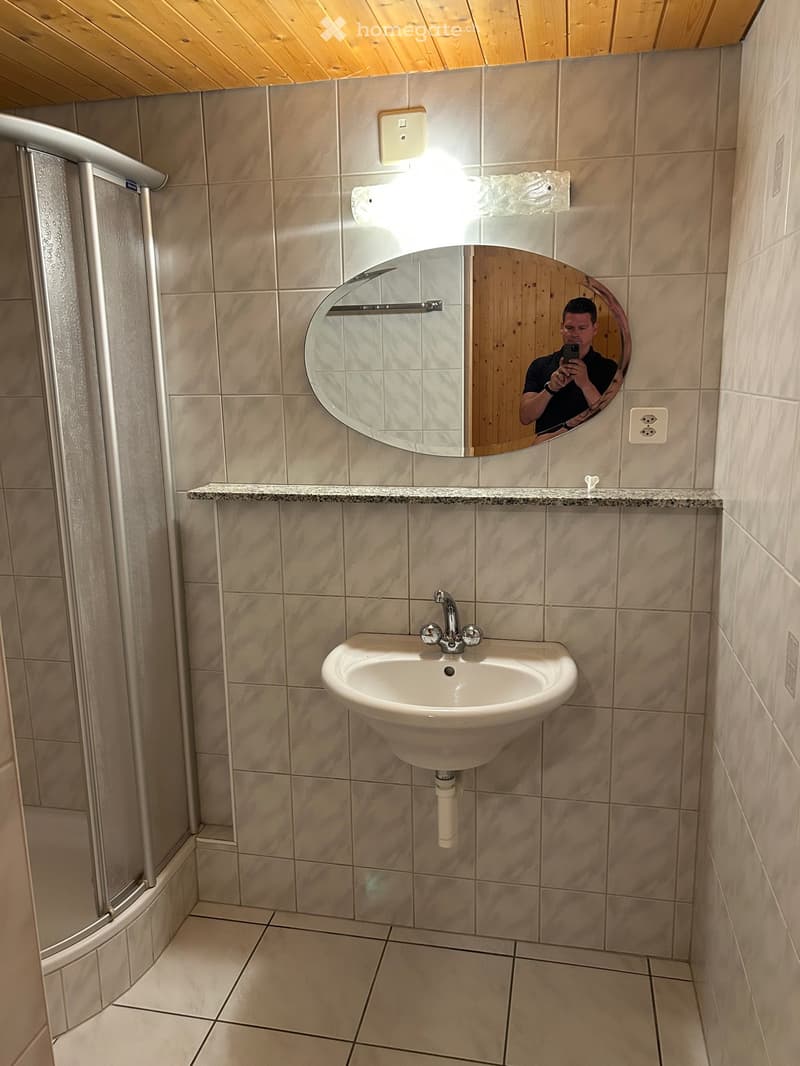 Bathroom with a white sink, chrome faucet, round mirror, and light fixture above the sink. Shower area visible on the left.
