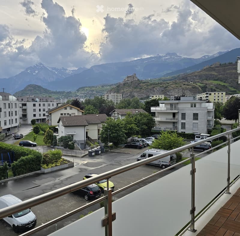 Balcony overlooking a parking lot, residential buildings, and a scenic mountain view.