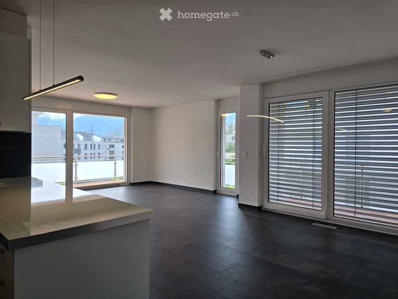 Empty room with dark tiled floor, white walls, large windows with blinds, and a small counter area.