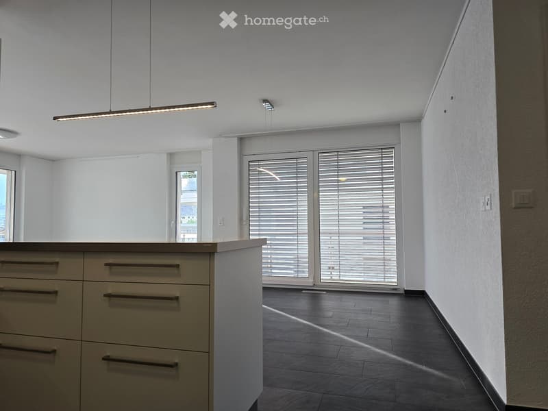 Modern kitchen with a light-colored island, pendant lighting, and large windows with blinds.