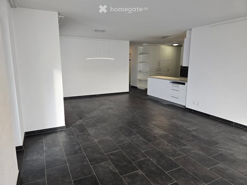 Empty room with dark tiled floor, white walls, and a modern kitchen area with white cabinets and a countertop.