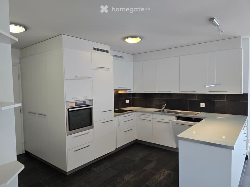 Modern kitchen with white cabinets, stainless steel appliances, dark tiled floor, and a central island.