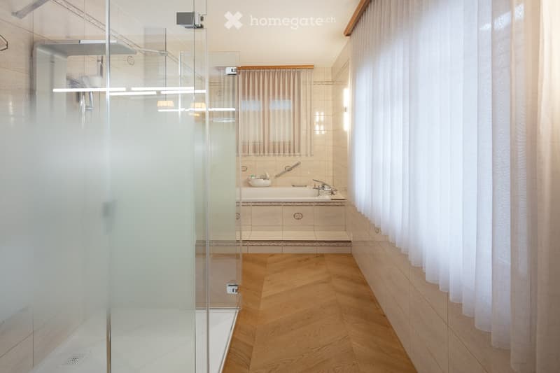 Modern bathroom with a bathtub, glass-enclosed shower, and wooden flooring.