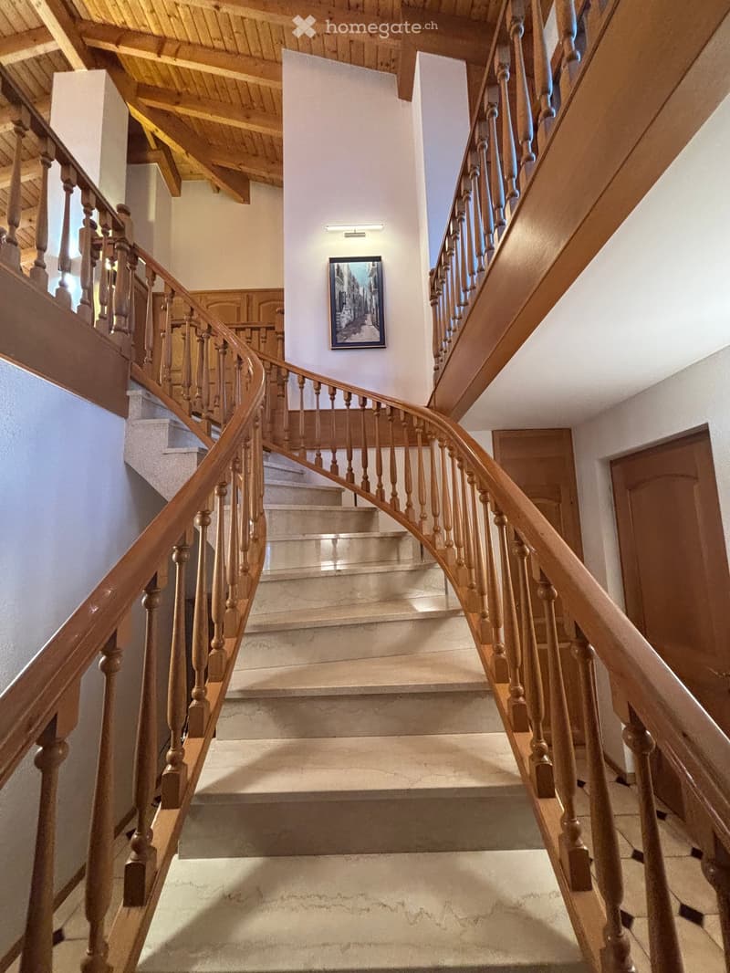 Spiral staircase with wooden handrails and balusters, beige walls, and a framed picture on the wall.