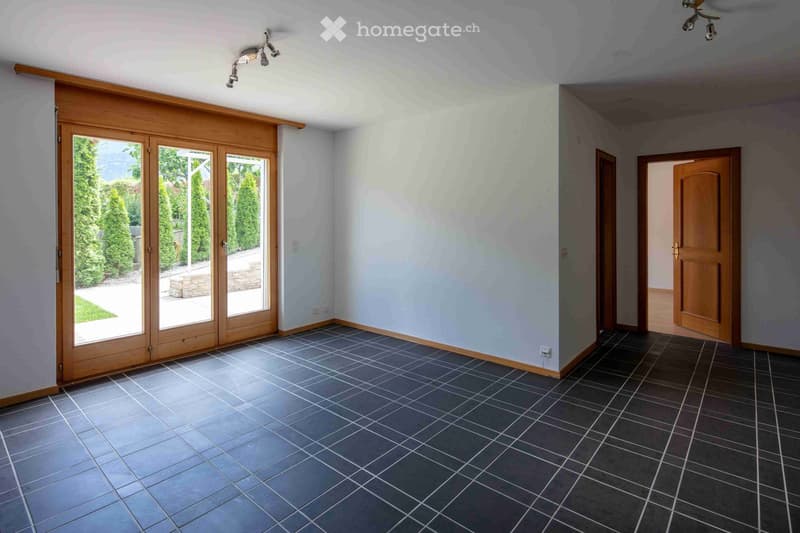 Empty room with grey tiled flooring, light grey walls, and wooden sliding doors leading to a garden area.