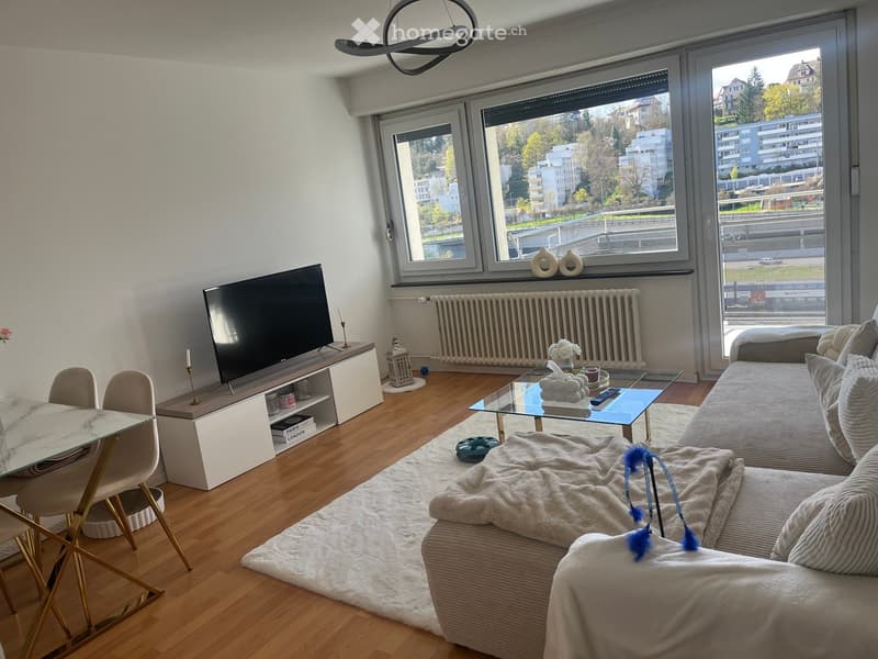 Modern living room with large windows, a sofa, coffee table, TV, dining table, and chairs.