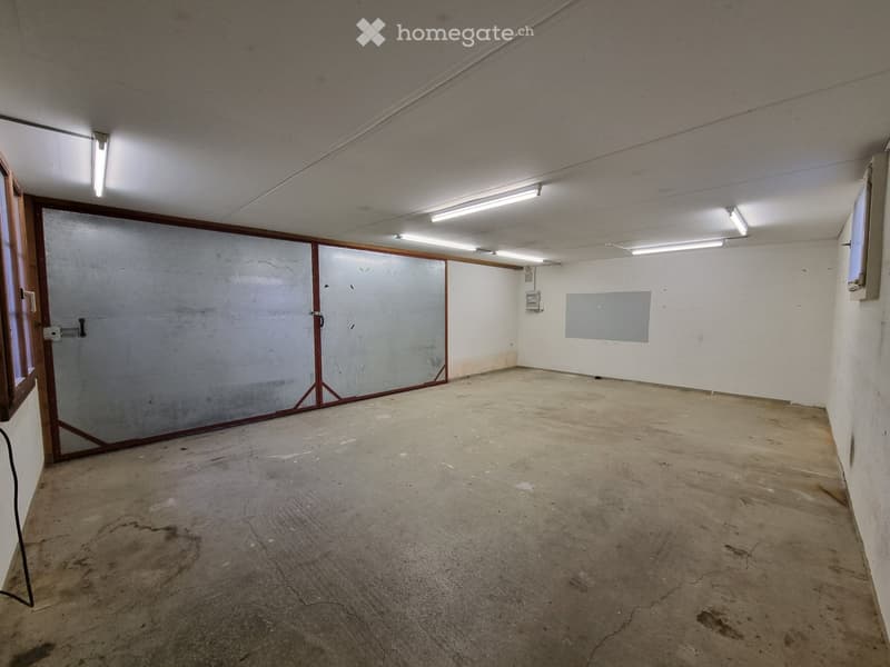 Empty room with concrete floor, metal doors, white walls, windows, and ceiling lights