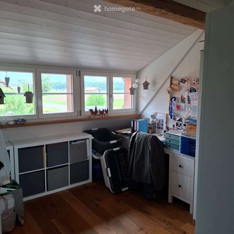 Furnished Room. Bright attic room with wooden floors, large windows, a desk with a chair, storage unit, and various decorative items.