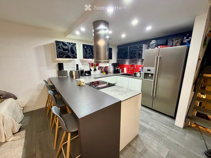 Modern kitchen with a central island, bar stools, stainless steel appliances, and a red backsplash.