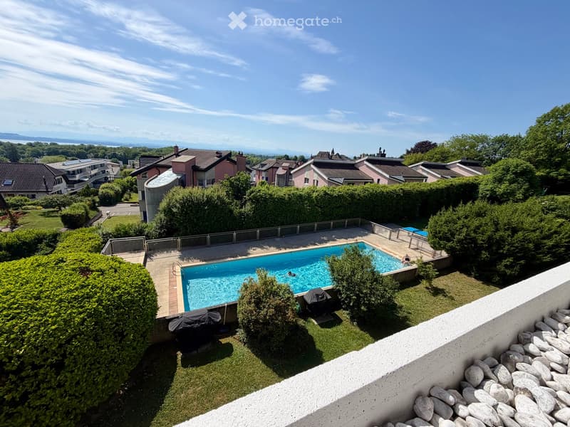A well-maintained garden with a swimming pool, surrounded by greenery and hedges, with a scenic view of the surrounding area and distant mountains.