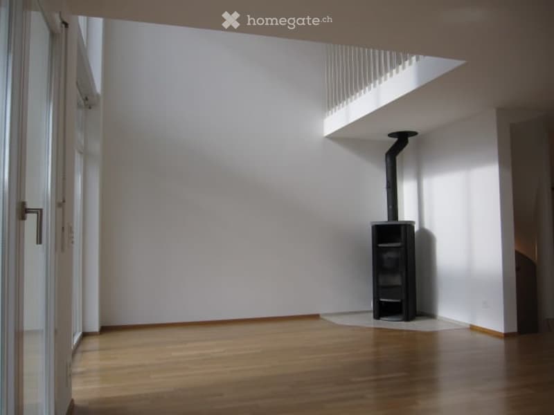 Empty room with wooden flooring, white walls, and a small black fireplace in the corner.