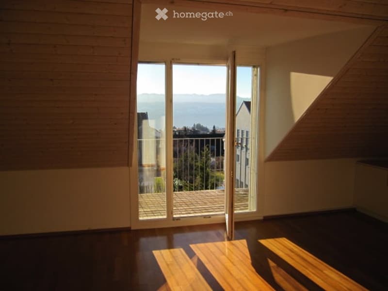 Open sliding glass doors lead to a balcony with a scenic view of the landscape and surrounding buildings.