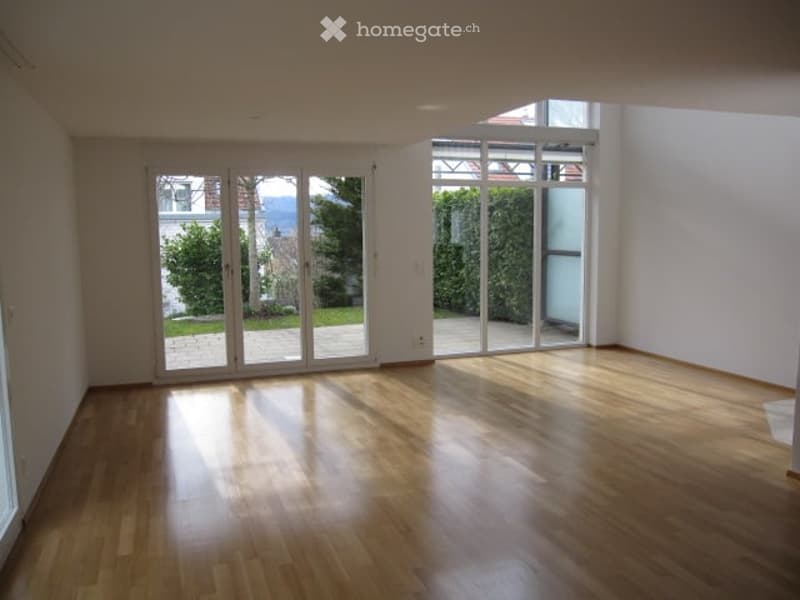 Empty room with wooden flooring and large glass sliding doors leading to a garden view.