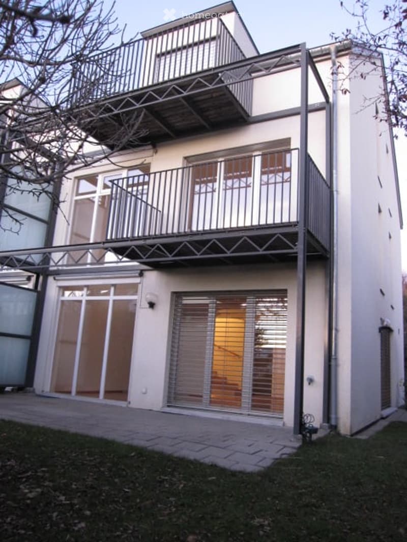 Modern two-story building with white exterior, large windows, and multiple balconies.