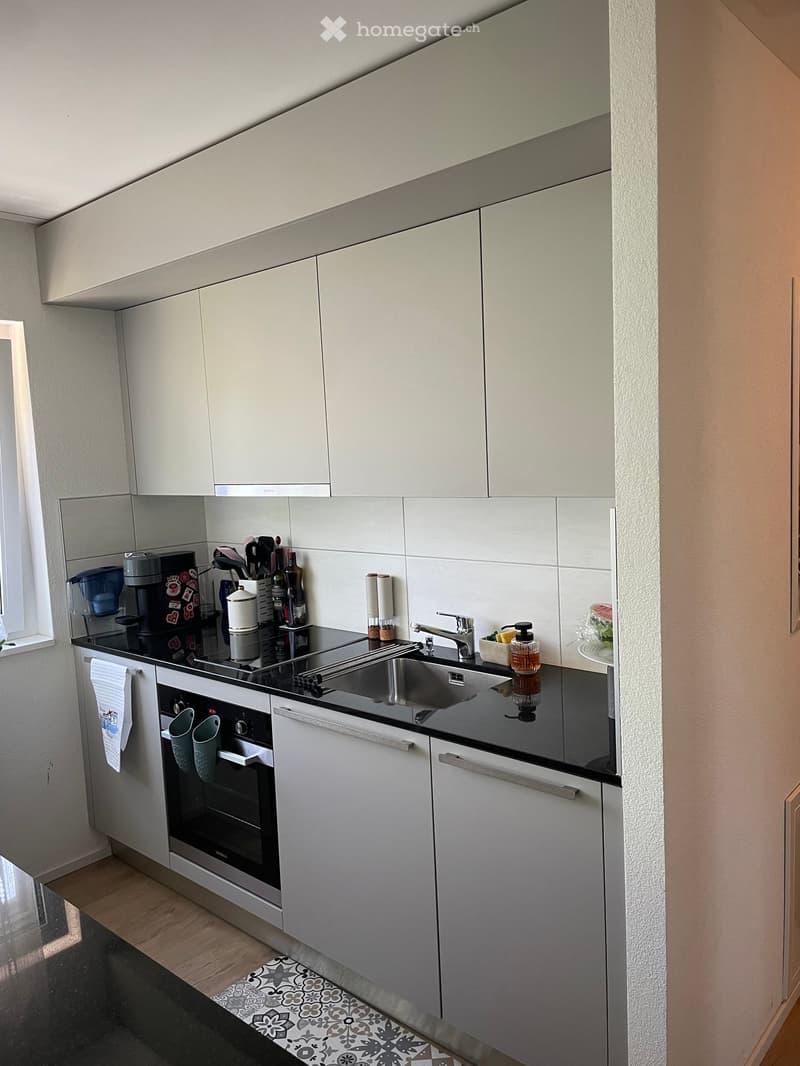 Modern kitchen with white cabinets, stainless steel appliances, and a black countertop. Features an oven, sink, coffee maker, and various kitchen utensils.