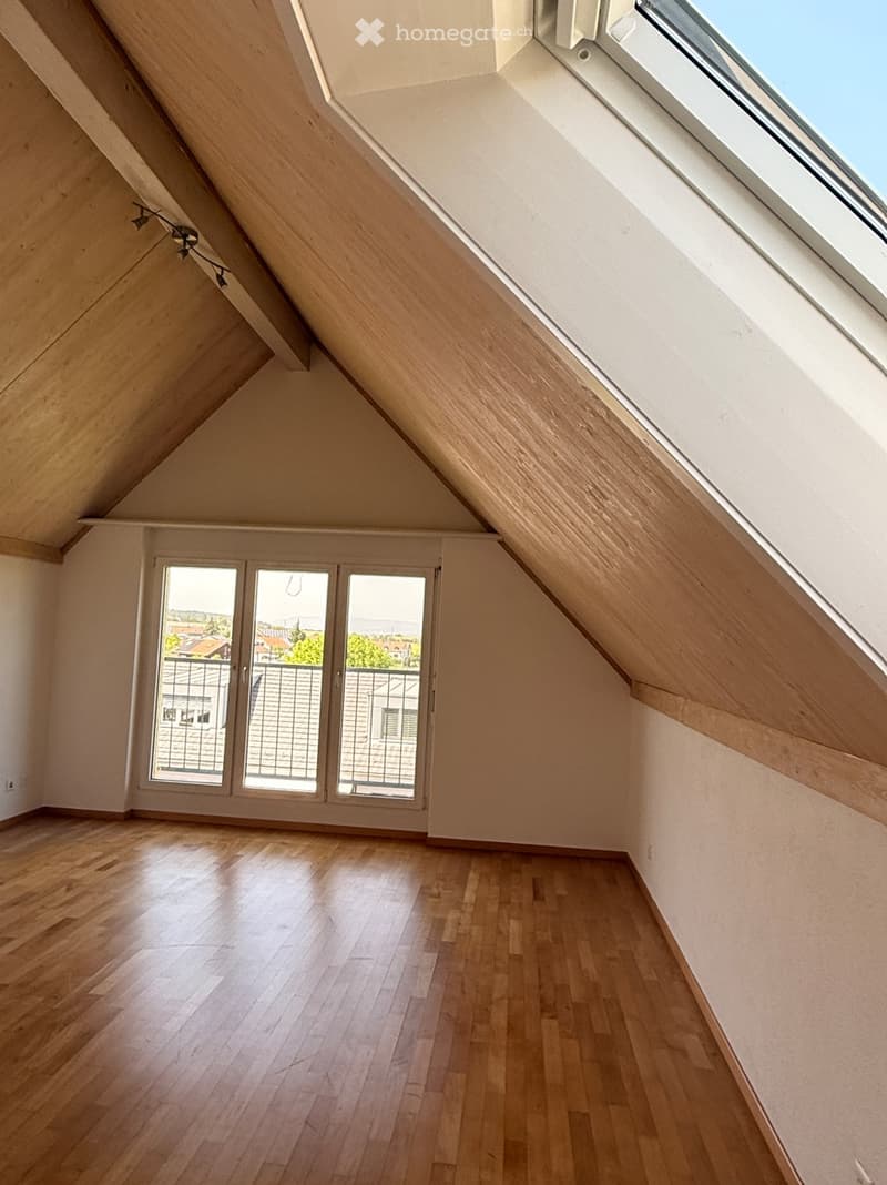 Empty attic room with wooden flooring, skylight window, and large sliding glass doors leading to a balcony.