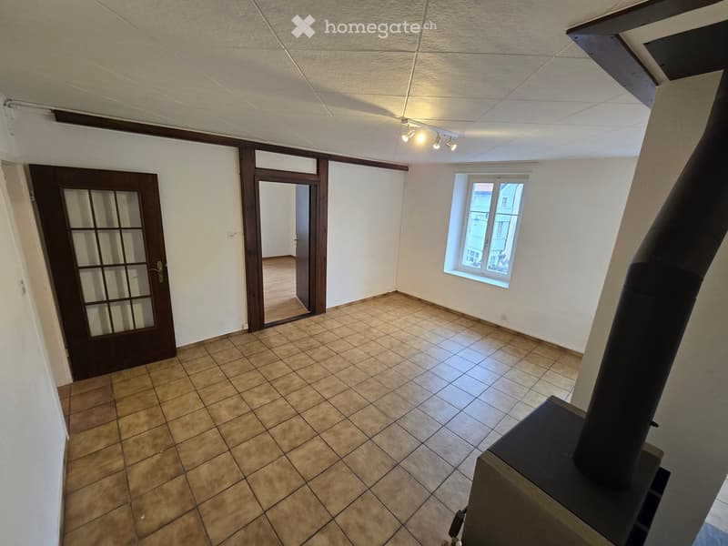 Empty room with tiled floor, white walls, a window, and a door leading to another room. A chimney is visible in the foreground.
