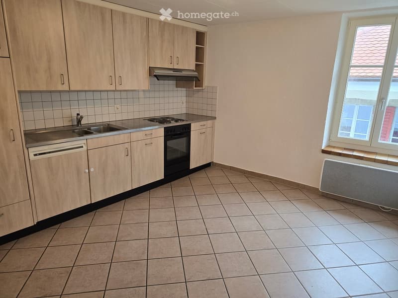 Empty kitchen with light wooden cabinets, tiled floor, sink, stove, oven, and dishwasher.