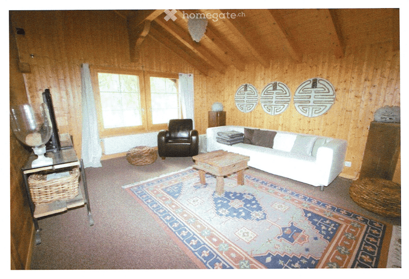 Cozy living room with wooden walls and ceiling, large windows, white sofa, dark armchair, wooden coffee table, and decorative mirrors.