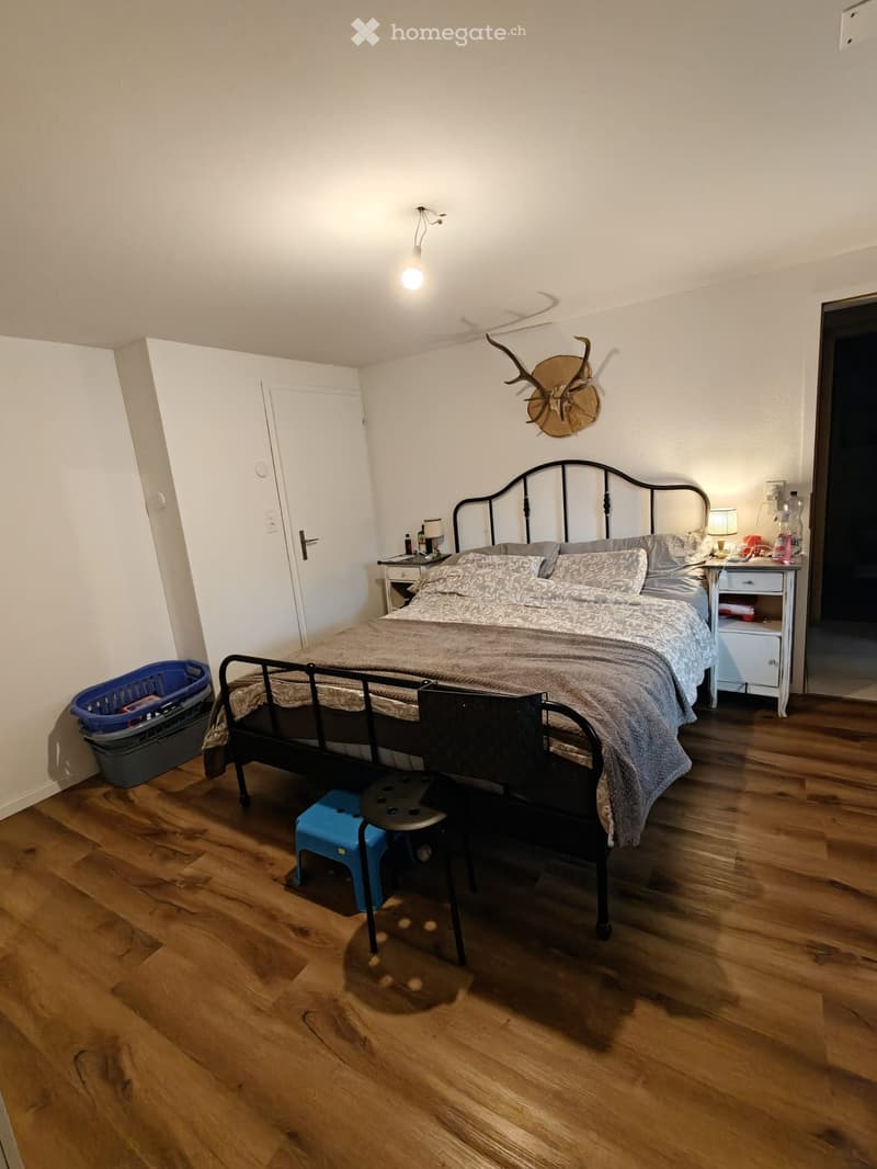 Cozy bedroom with wooden flooring, a metal-framed bed, nightstands, a deer head wall decoration, and a small stool near the bed.
