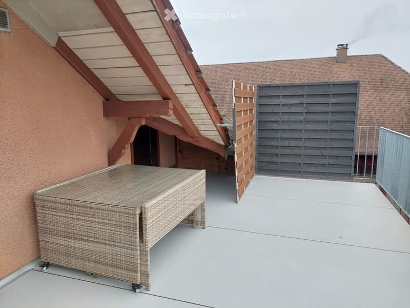 Balcony with a wicker sofa, wooden shutters, and a view of a neighboring building.