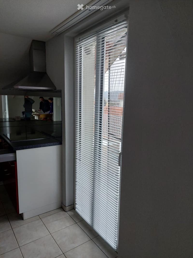 Modern kitchen with white cabinets, a central island, and a large window with white blinds. A stainless steel range hood is visible above the cooking area.