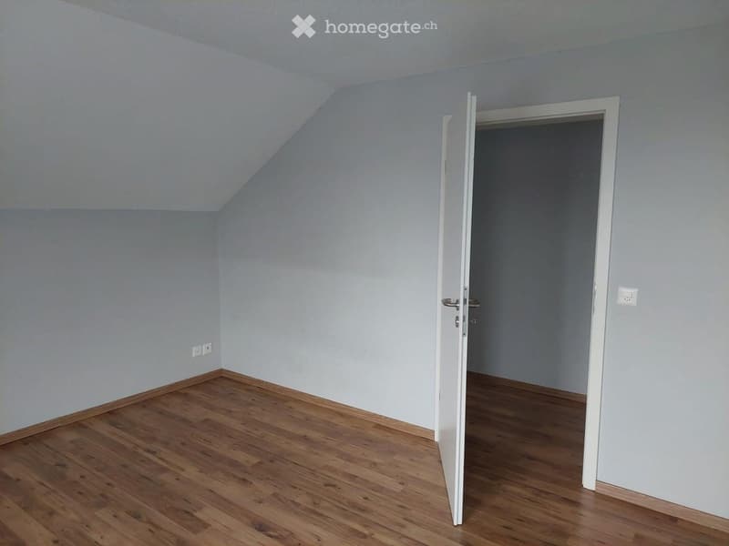 Empty room with wooden flooring, light grey walls, and an open door leading to another room.