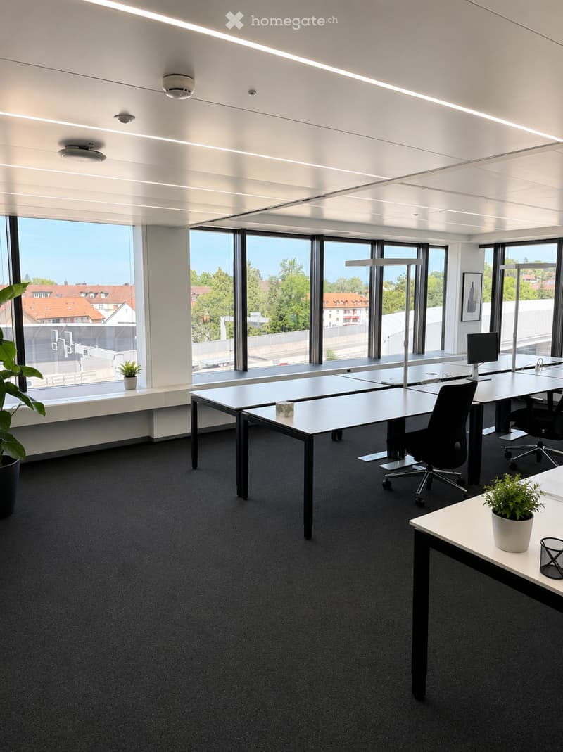 Modern office space with large windows, desks, chairs, and plants.