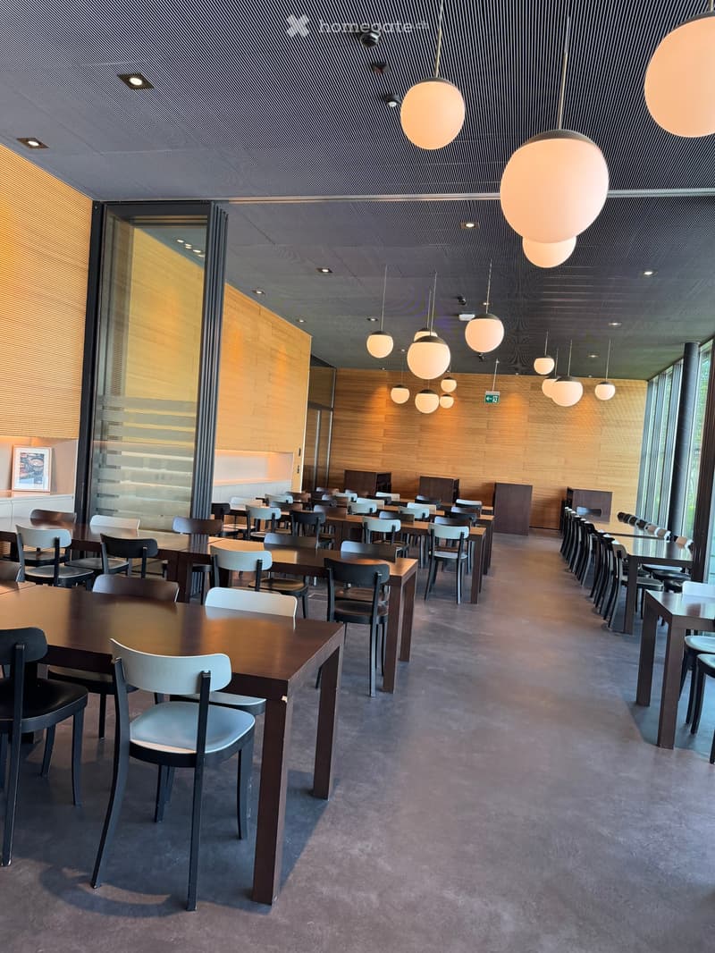 Modern dining area with multiple tables and chairs arranged in rows, large pendant lights, and a sleek, contemporary design with wooden paneling and glass walls.
