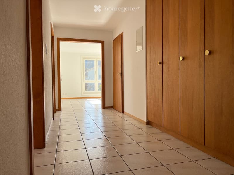 Empty hallway with tiled floor, wooden doors, and a view into a room with a window.