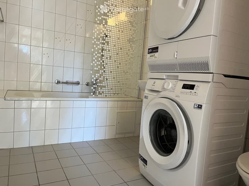 Modern bathroom with white tiled walls, a shower area, a washing machine, and a bathtub.
